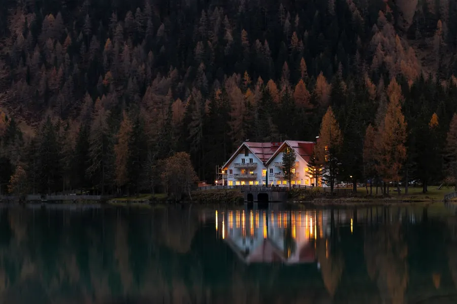 Casa iluminada junto a un lago rodeado de bosque (foto referencial)